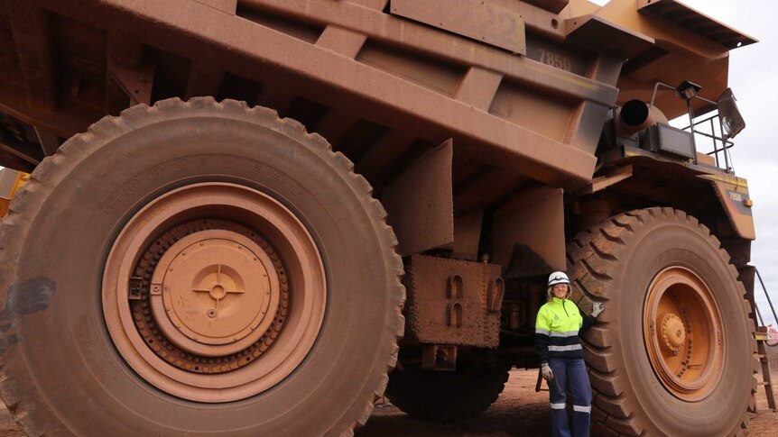 Big mining truck with woman in high vis gear and helmet standing by large tyre on the left