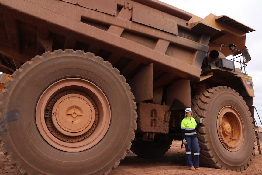 Big mining truck with woman in high vis gear and helmet standing by large tyre on the left