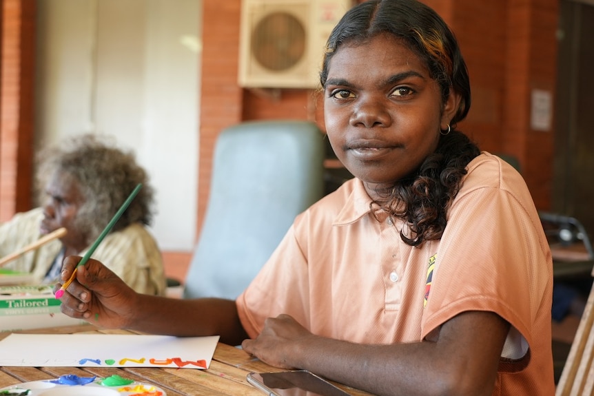 A young Aboriginal woman sits smiling at a table