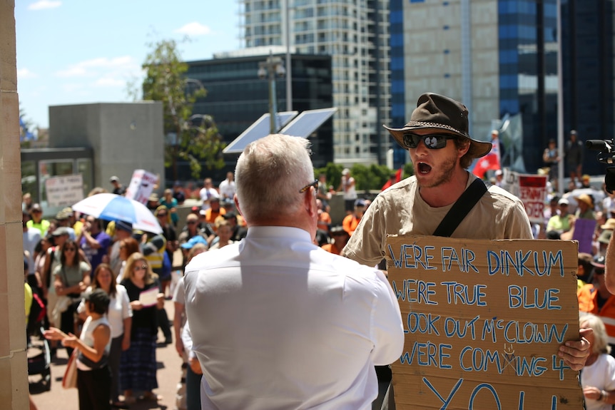 A man in a hat yells in the face of a man in a white shirt with a crowd in the background