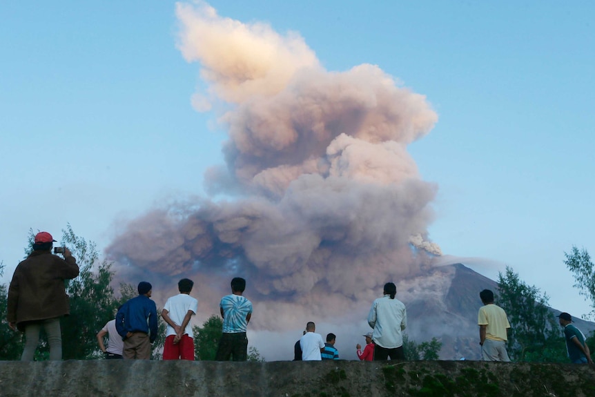 Residents watch as Mayon volcano spews smoke and ash