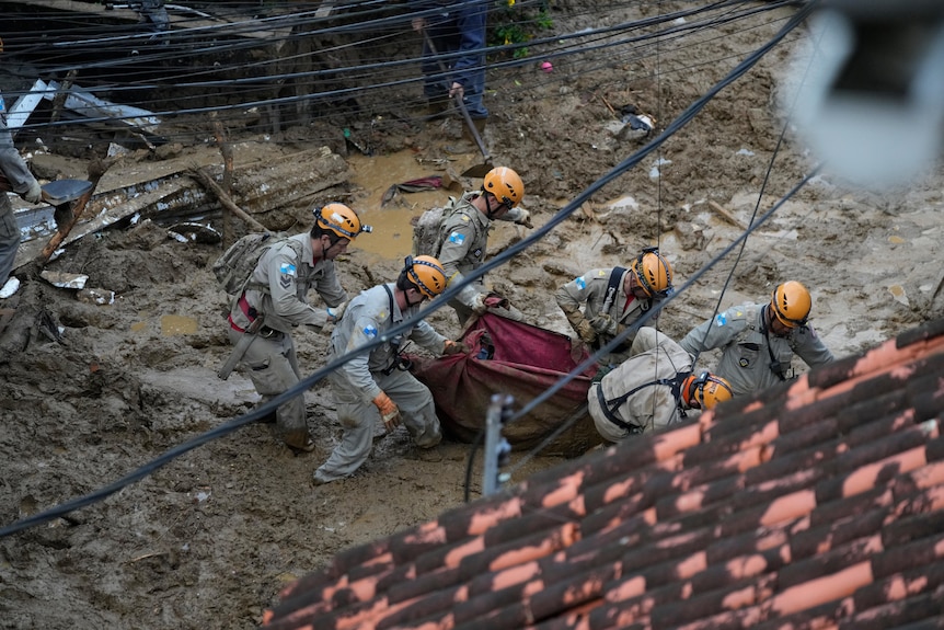 Rescue workers carry the body of a landslide victim through ankle high mud.