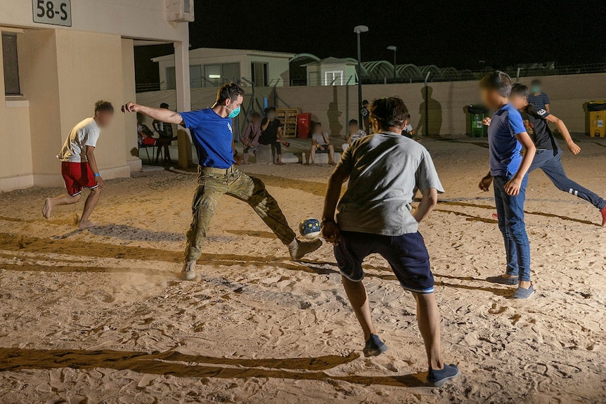 Un soldat en chemise bleue joue au football avec de jeunes enfants afghans.