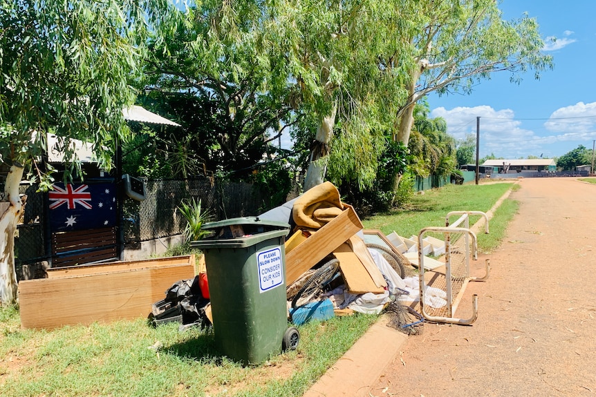 Household furniture and other items sit next to a bin on the curb of a suburban street