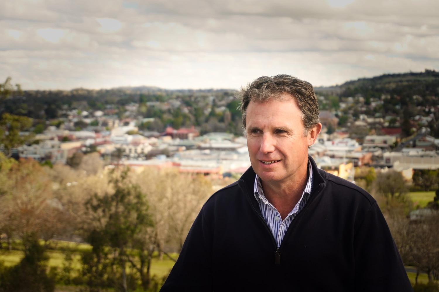 A portrait photo of a man staring away form the camera with houses in the background