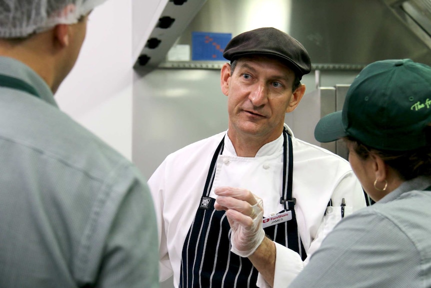 James Fien in a chef's uniform chats to volunteers.