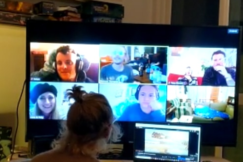 A group of people gather on Zoom, multiple people on screen, one person looking in the room.