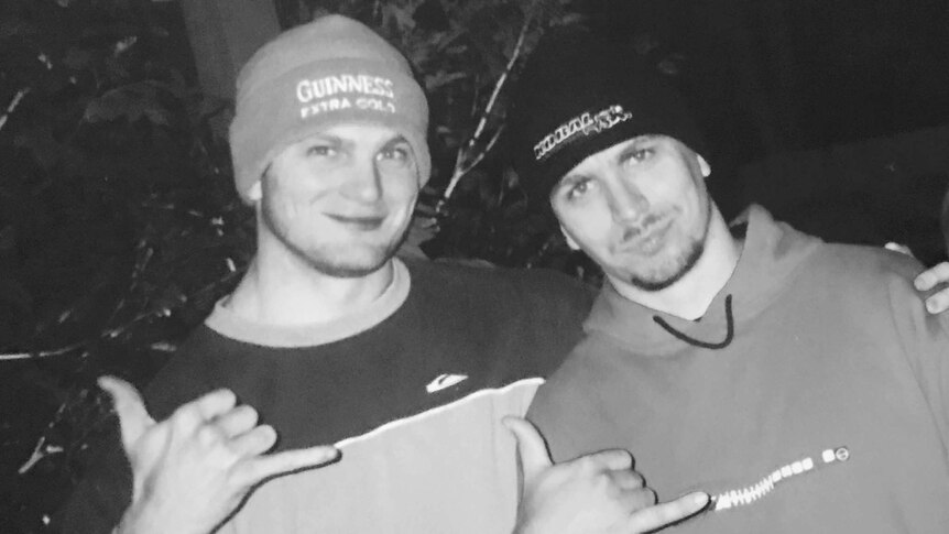 Black and white photo of two men in their 30s wearing beanies and smiling at the camera.