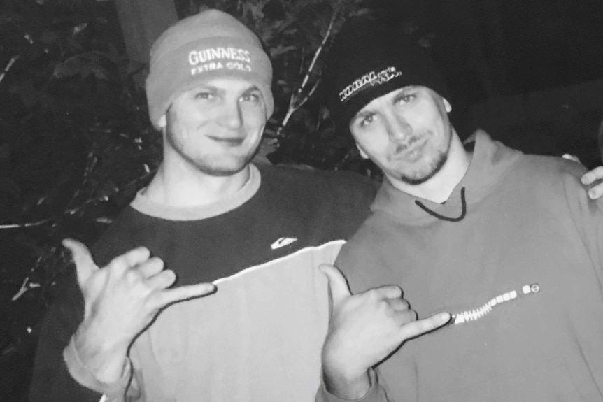 Black and white photo of two men in their 30s wearing beanies and smiling at the camera.