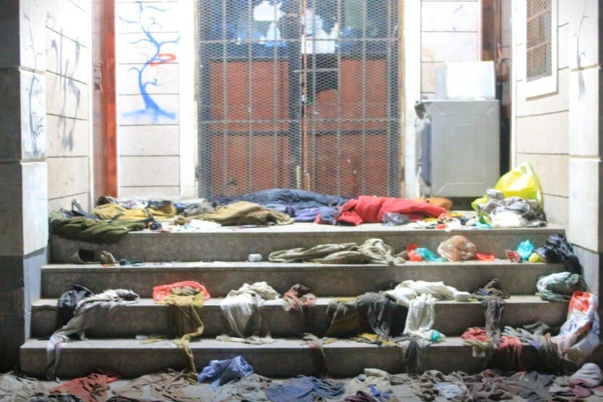 Multi-coloured clothes lie strewn on the steps in a brightly lit room.