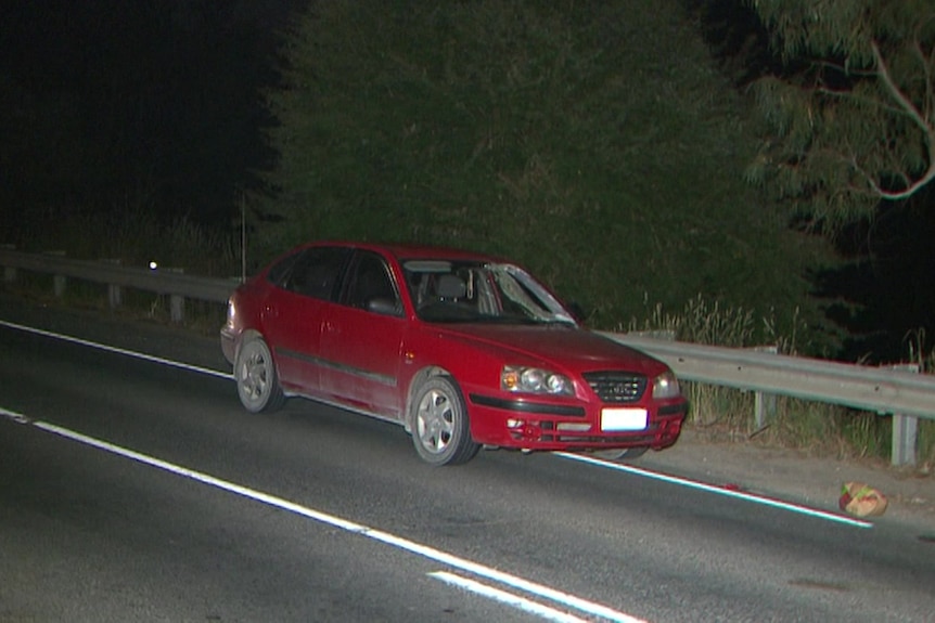 A red car next to a barrier on the side of a road