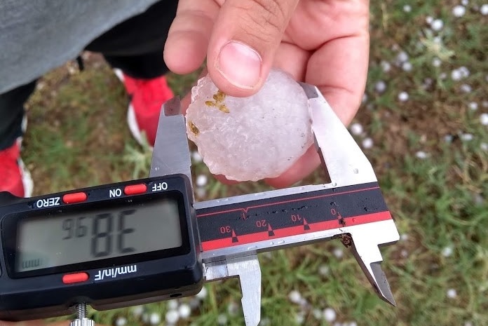A man holds a hail stone against a measuring implement.