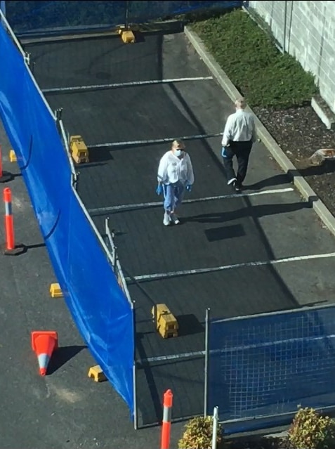 Two people in face masks walking within a fenced off area in a hotel car park.