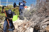 police with shovels search dunes with ocean in the background