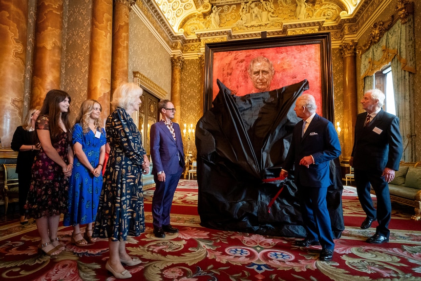 King Charles pulling a black sheet off a big frame with others standing around