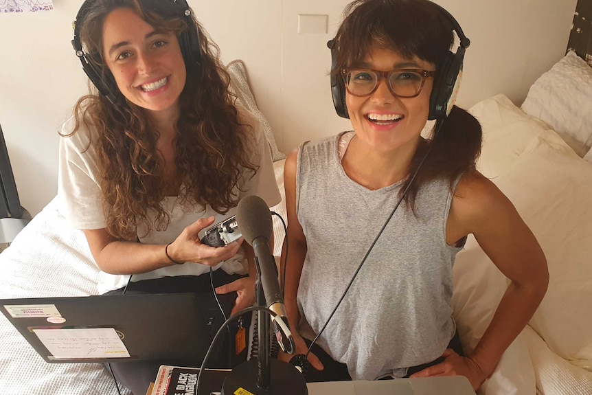Two women sitting next to one another wearing headphones and holding a mic.