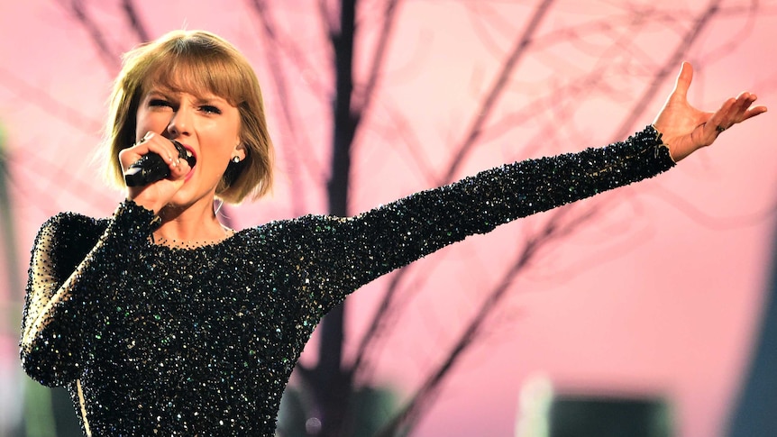 Upper body photo of Taylor Swift, one arm outstretched beside her performing at the Grammy Awards.