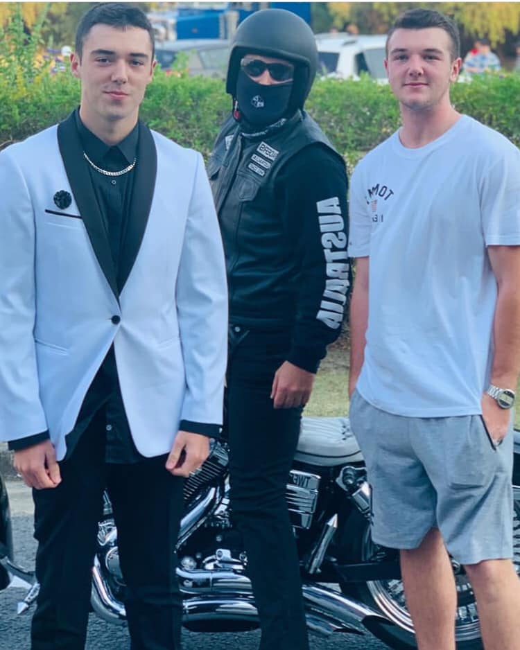 A teenager in a formal suit poses with two other males.