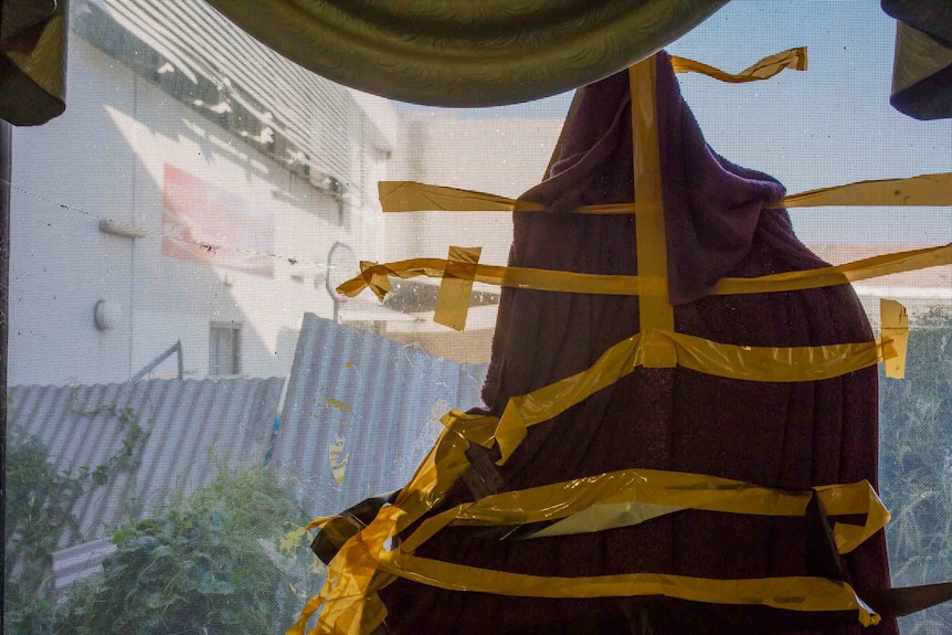 Purple fabric is taped to a broken window with yellow sticky tape.