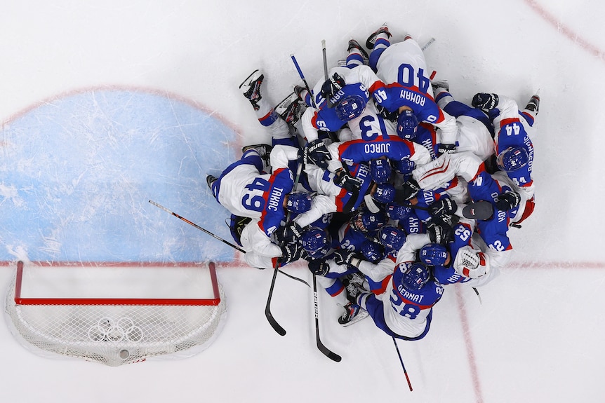 An entire Olympic ice hockey team pile on top of each other in celebration on the ice after winning a game.