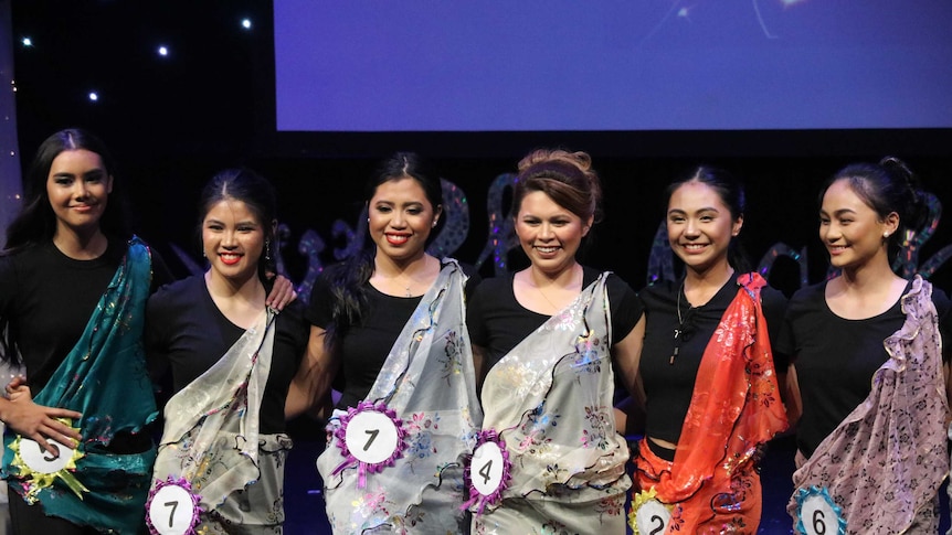 Six young women stand on a stage