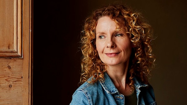 A middle-aged white woman with long curly red hair and wearing a denim jacket