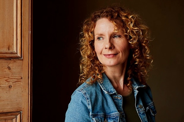 A middle-aged white woman with long curly red hair and wearing a denim jacket