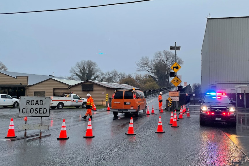 Emergency vehicles with traffic cones around a road with a road closed sign