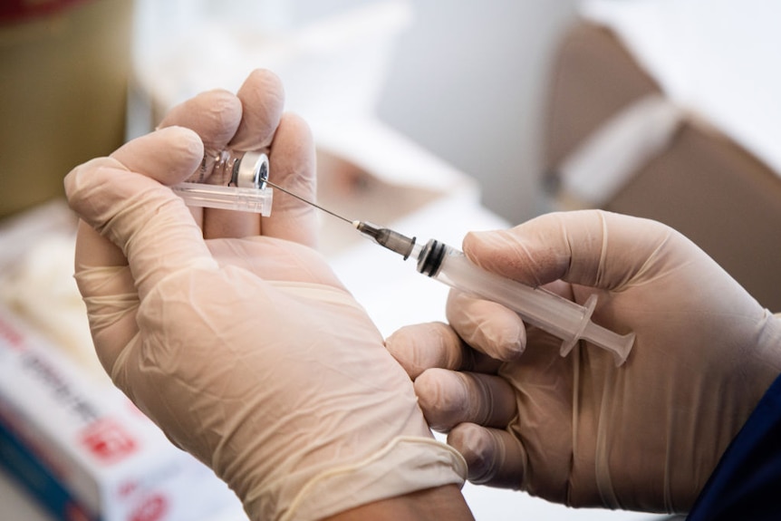 A nurse holds a vaccination syringe and a vial of a COVID-19 vaccine.