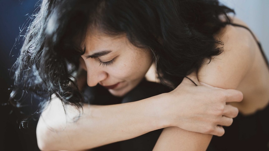 A woman with a pained expression hugs herself