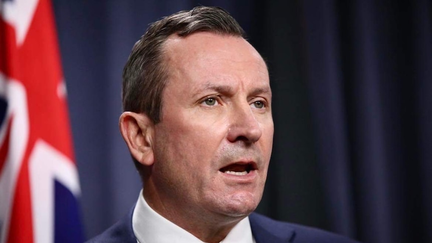 A man with short hair and a blue jacket delivers a speech at a lectern