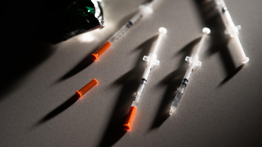 Generic syringes of compounded replica Ozempic lying across a shadowy table.