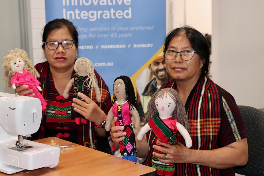 Two women from Myanmar pose for a photo next to a sewing machine holding up fabric dolls made in a craft class.