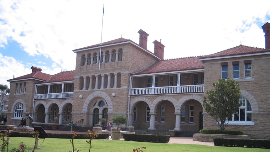 A stately sandstone civic building with a cleanly manicured garden in front.