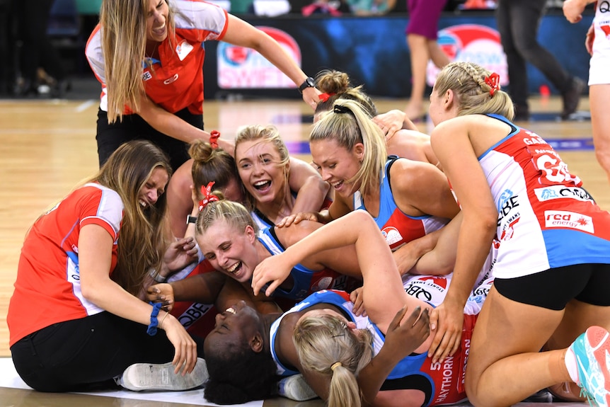 Swifts players pile on each other on the court, smiling and laughing