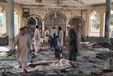 People view the damage inside of a mosque covered in debris with blood stains marking the floor.
