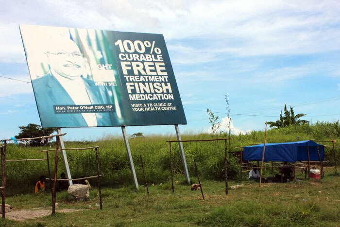 A makeshift shelter next to a TB billboard featuring the Prime Minister, Peter O'Neill.