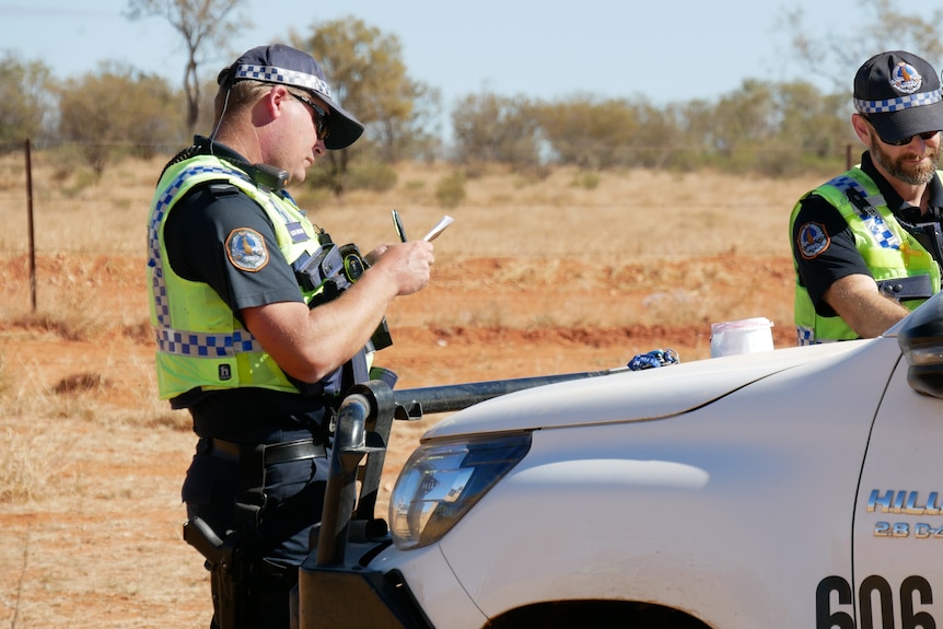 Two police officers stand by their car in the desert. 