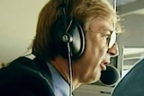 Wearing a headset microphone, Dennis Cometti calls a game.