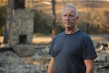Greg Mullins stands next to the ruins of a burnt out building.
