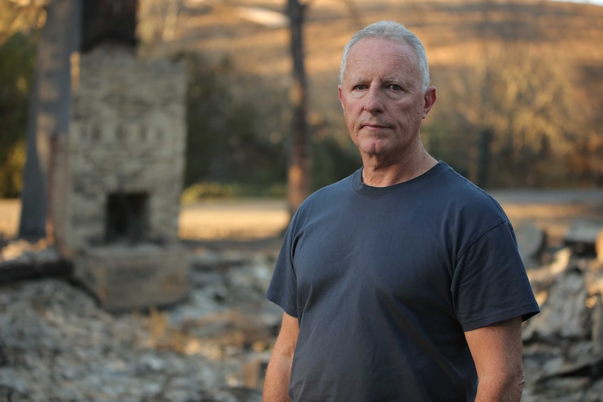 Greg Mullins stands next to the ruins of a burnt out building.