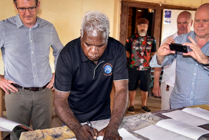 Tony Wurramarrba signs a document on a table in front of press.