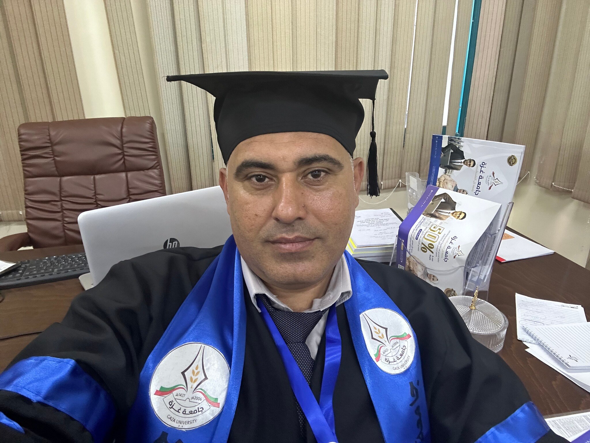 A man dressed in a graduation cap and gown, with blue ribbons. 