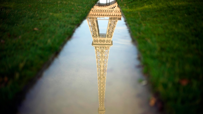 The Eiffel tower is reflected in water along the Champs de Mars.