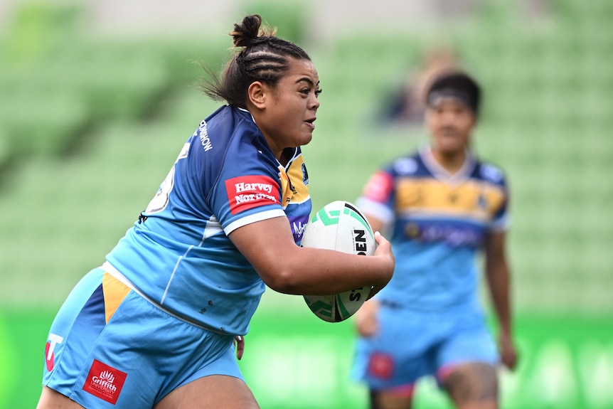 A Gold Coast Titans NRLW player holds the ball as she runs at the Parramatta Eels defensive line.