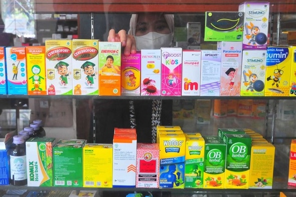 Glass shelves filled with medicines, mostly in syrup form at a pharmacy in Indonesia.