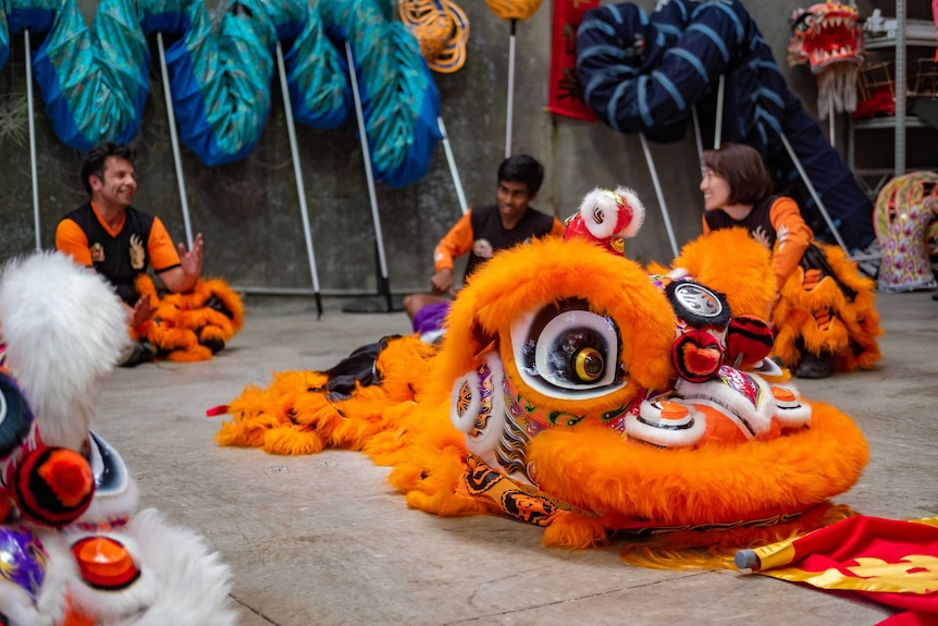 Two male and a female performer sitting on the ground taking a break during lion dance practice.