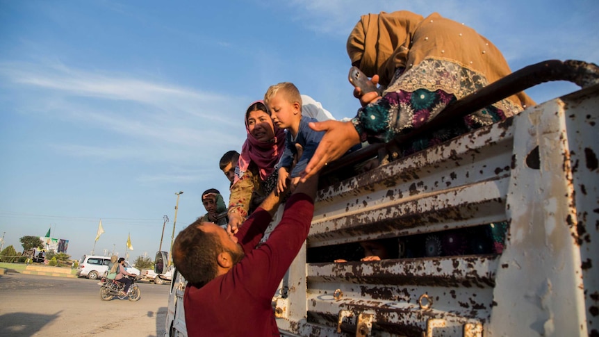 A man helps Syrians fleeing Turkish advance climb down from the back of a truck.