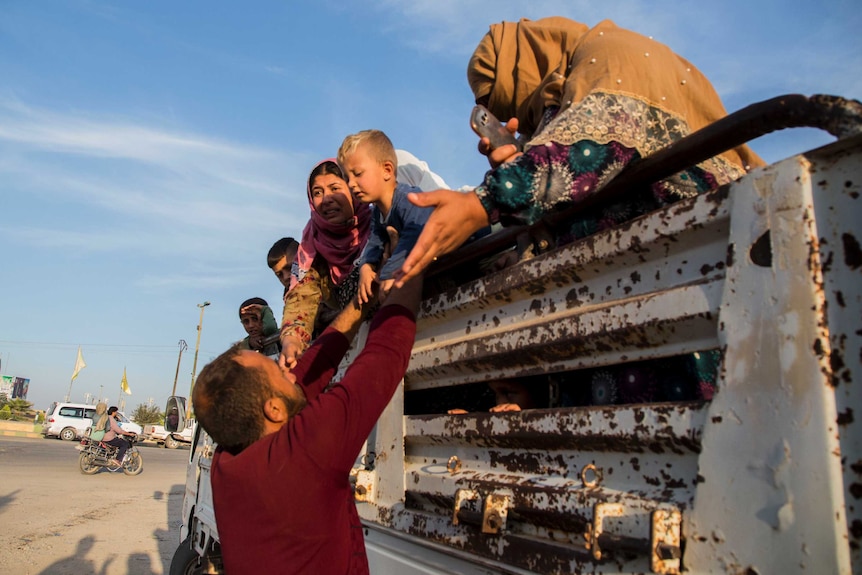 A man helps Syrians fleeing Turkish advance climb down from the back of a truck.