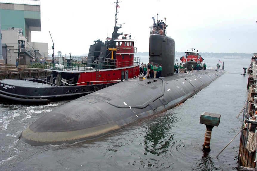 Un sous-marin nucléaire en surface à quai à côté d'un remorqueur. 
